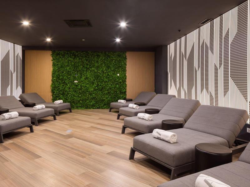 Ruheraum mit grauen Liegen, Holzboden und grüner Pflanzenwand am Ende des Raumes.