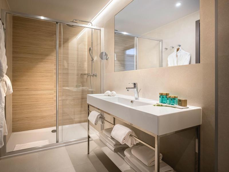 Moderne Dusche mit Glaswand, Holzfliesen, großem Spiegel, weißem Waschtisch und Handtüchern.