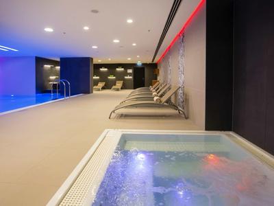 Area benessere moderna con vasca idromassaggio, piscina e lettini sotto luce calda.