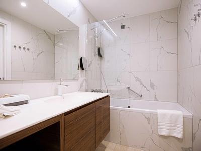 Bagno moderno con mobili in legno, grande specchio, vasca da bagno e piastrelle bianche.