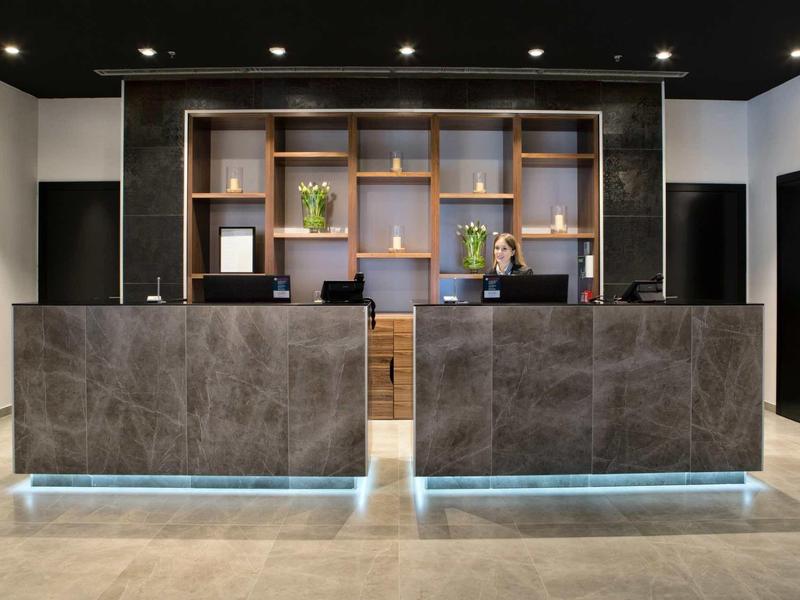 Reception di un hotel moderno con due banconi, scaffali in legno e personale cordiale.