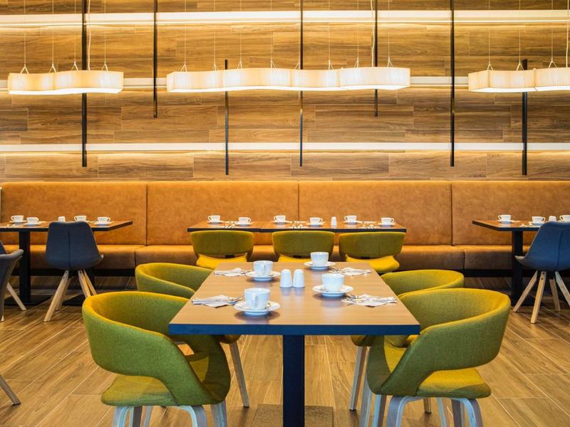 Ristorante moderno con sedie verdi e blu, tavoli apparecchiati e illuminazione calda.