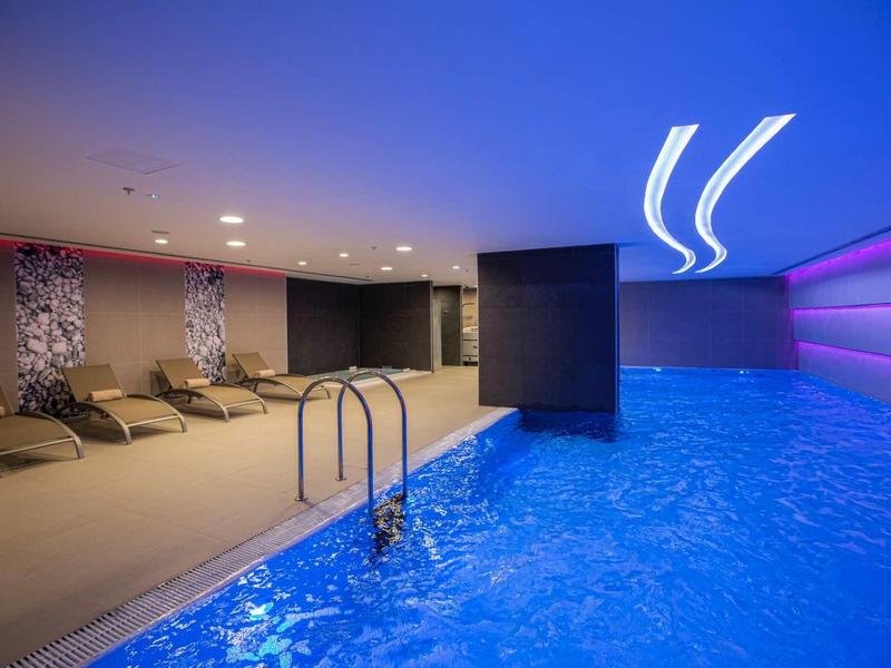 Piscina interna moderna con illuminazione blu e sedie a sdraio in un ambiente elegante.