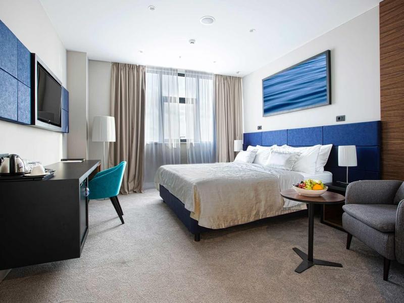 Camera d'hotel moderna con letto matrimoniale, scrivania, poltrone e finestra grande