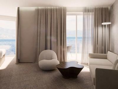 Modern living room with sea view, sofa, armchair, and large windows with curtains.