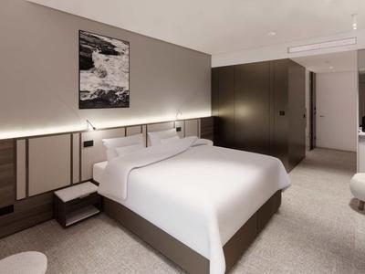 Modern hotel room with large double bed, neutral color scheme, and indirect lighting.