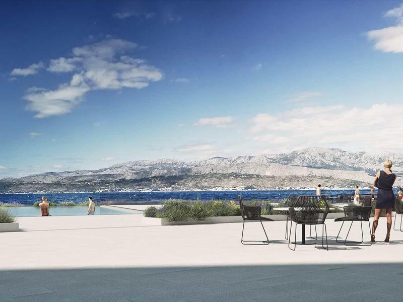 Terrace with tables and chairs overlooking the sea and a mountainous landscape in sunshine.