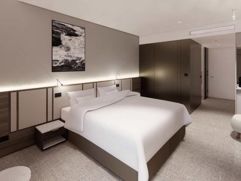 Modern hotel room with large double bed, neutral color scheme, and indirect lighting.