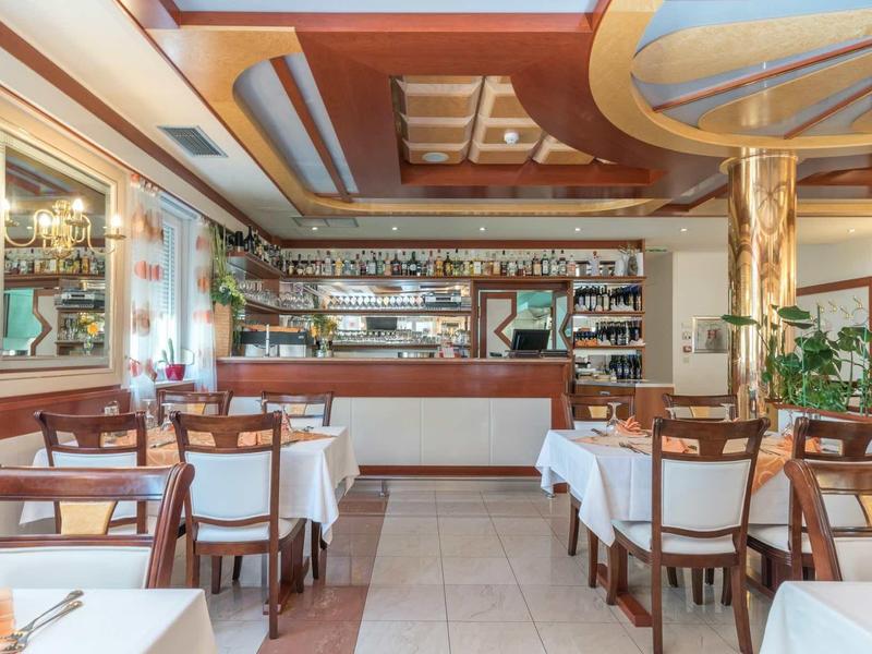 Restaurant élégant avec mobilier en bois, nappes blanches et un grand bar en arrière-plan.