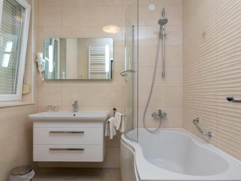 Salle de bains moderne avec baignoire, meuble lavabo, grand miroir et carreaux muraux clairs.