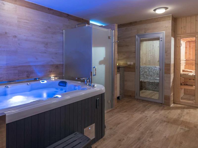 Espace bien-être moderne avec jacuzzi, douche et sauna aux tons chauds de bois.