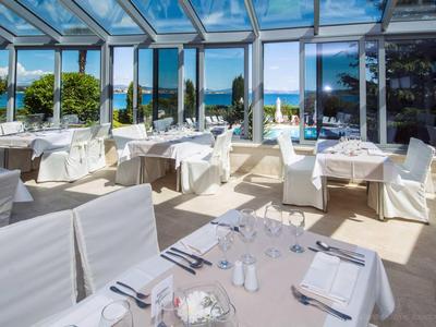 Terrasse de restaurant moderne et lumineuse avec chaises et tables blanches, vue sur jardin et mer.