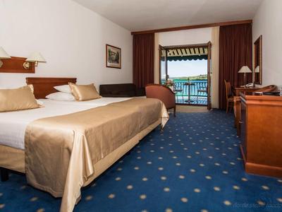 Chambre d'hôtel avec lit double, moquette bleue et balcon avec vue sur la mer.
