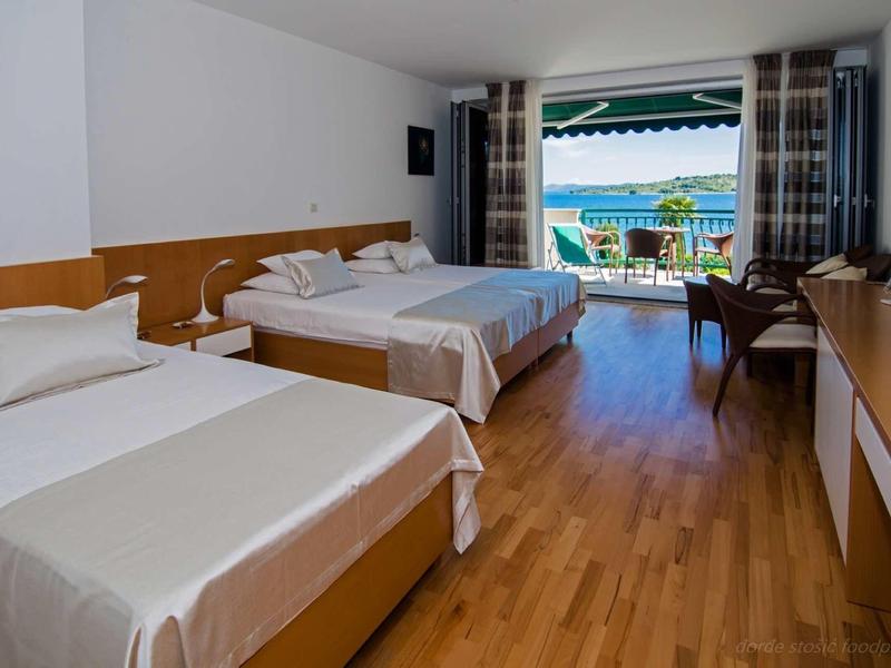 Bright hotel room with two beds, wooden floor, and balcony with sea view.