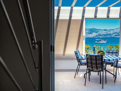 Moderne buitenruimte met zwarte metalen tafel en stoelen, uitzicht op zee en groene heuvels.