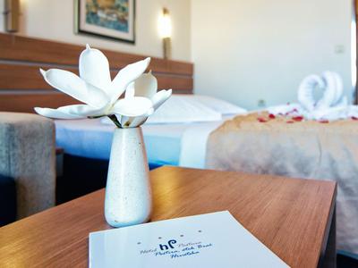 Close-up van een hotelkamer met een bloem op de tafel en een comfortabel bed op de achtergrond.