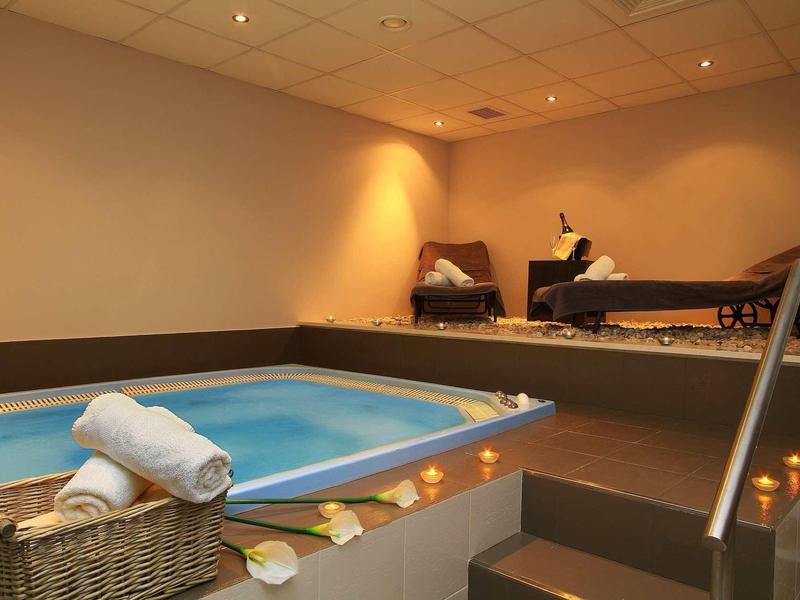 Wnętrze spa z jacuzzi, wiklinowym koszem i leżakami w przytulnym otoczeniu.