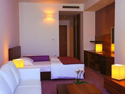 Nowoczesny pokój hotelowy z sofą, dwoma łóżkami, biurkiem i ciepłym oświetleniem.
