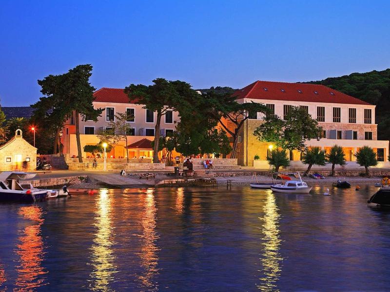 Verlicht hotel en boten aan de oever bij schemering met reflecties in het water.