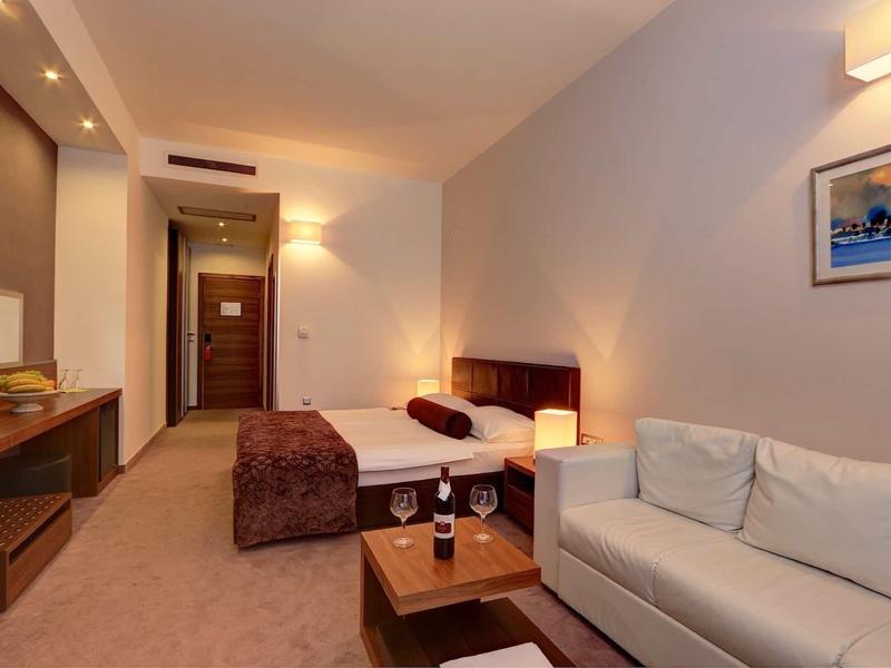 Gezellige hotelkamer met bed, bank en tafel met twee glazen.