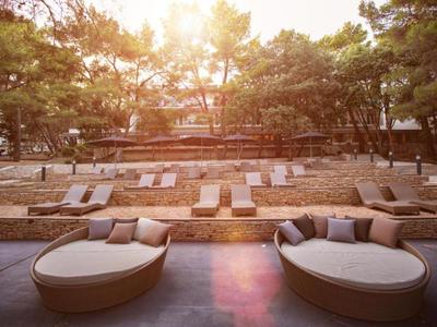 Außenbereich eines Hotels mit Sonnenliegen und Garten bei Sonnenlicht.