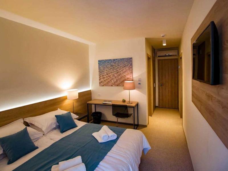 Moderně zařízený hotelový pokoj s manželskou postelí, psacím stolem a televizí s plochou obrazovkou.