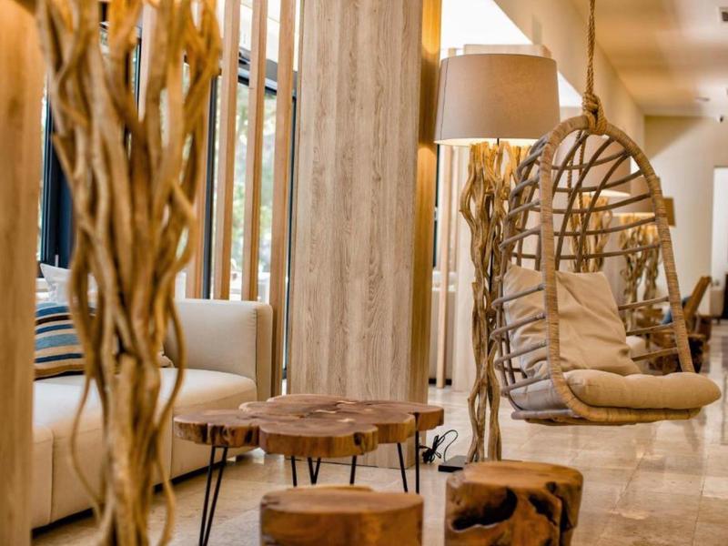 Světý hotelový pokoj s houpacím křeslem, stolky z dřevěných plátů a přírodní dekorací.