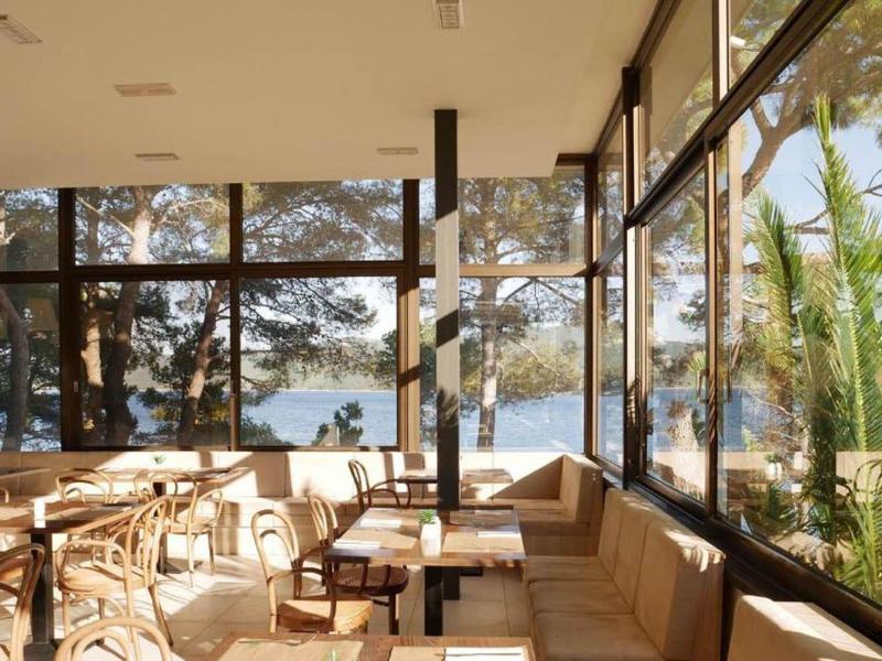 Světla restaurace s velkými okny s výhledem na moře a zelené rostliny.