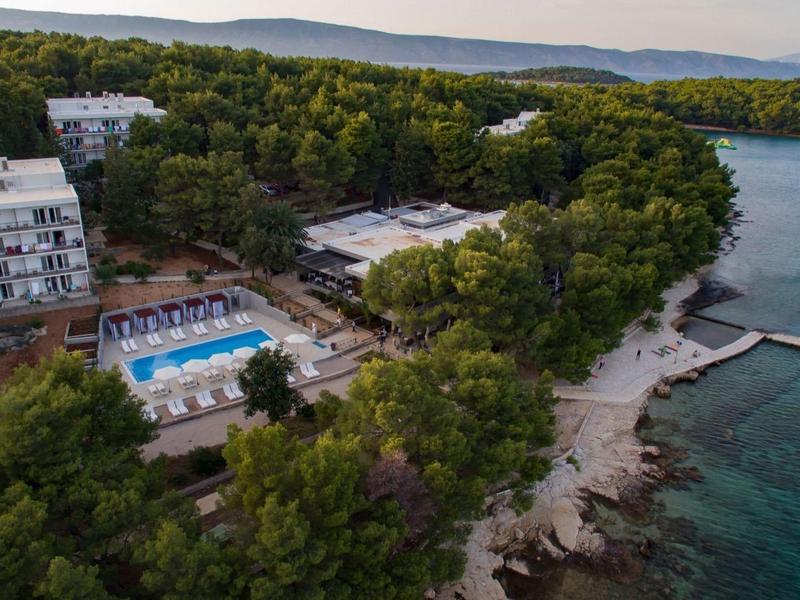 Hotelový komplex s bazénem na zalesněném pobřeží s molem a čistou vodou