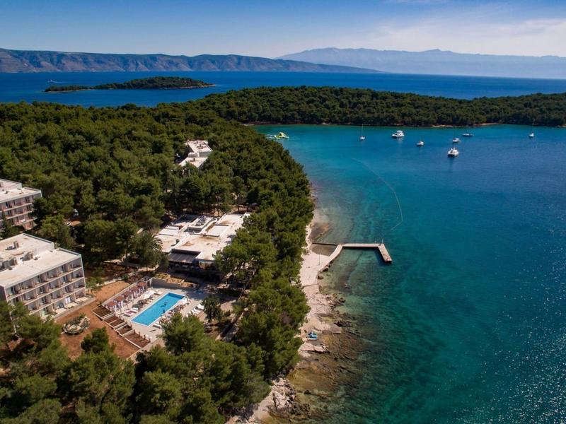 Letecký pohled na hotel u moře obklopený lesem s bazénem a molem.