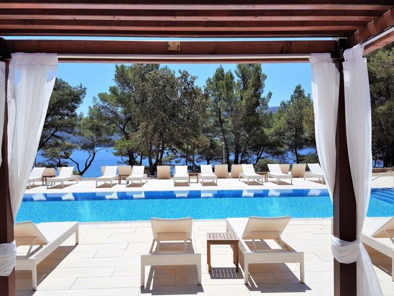 Bazénová oblast s lehátky a výhledem na moře pod zastřešenou terasou.