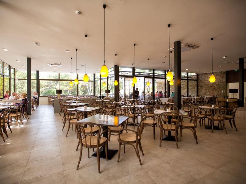 Velká světlá jídelna s dřevěným nábytkem a žlutými závěsnými lampami v hotelu.