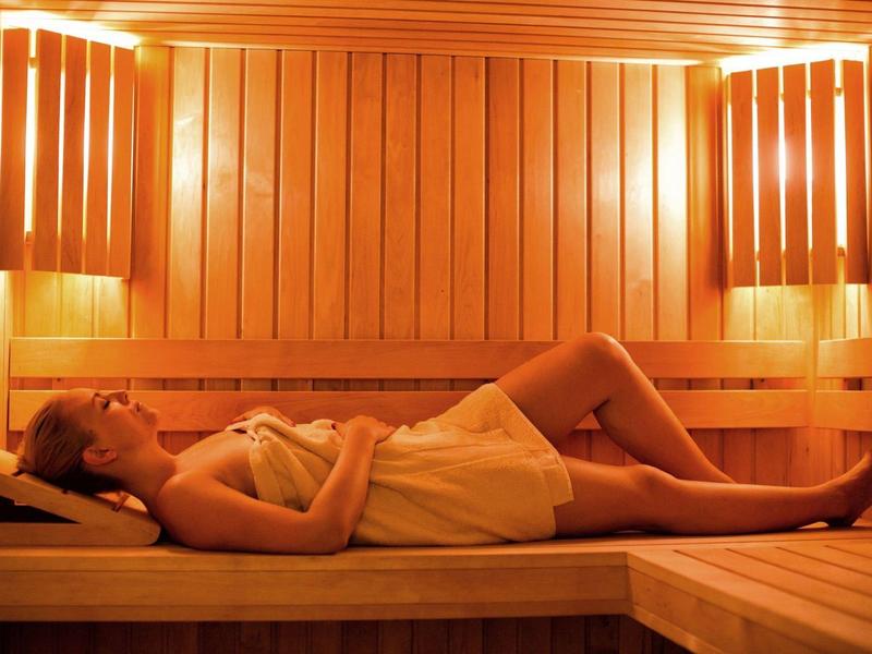 Žena relaxuje vleže v teplé osvětlené dřevěné sauně.