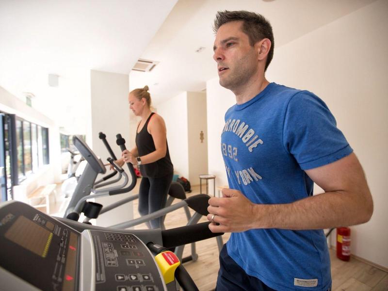 Dva lidé cvičí na běžeckých pásech v světlé posilovně.