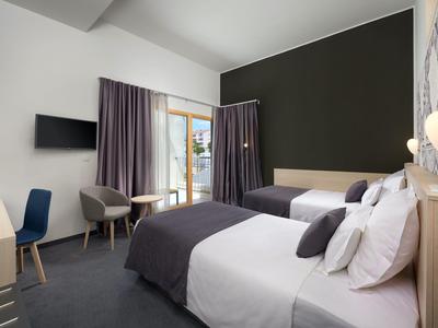 Modernes Hotelzimmer mit zwei Betten, Schreibtisch, Stühlen und Balkon mit Blick nach draußen.