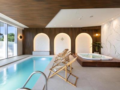 Moderner Wellnessbereich mit Pool, Whirlpool, Liegestühlen und stilvollen Wandleuchten.