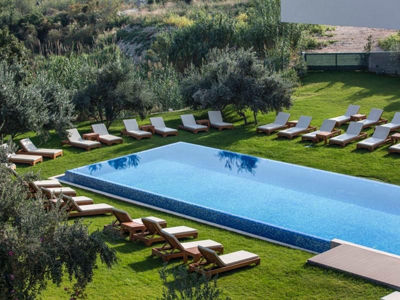 Langer Außenpool umgeben von Liegestühlen auf Rasenfläche mit Bäumen im Hintergrund.