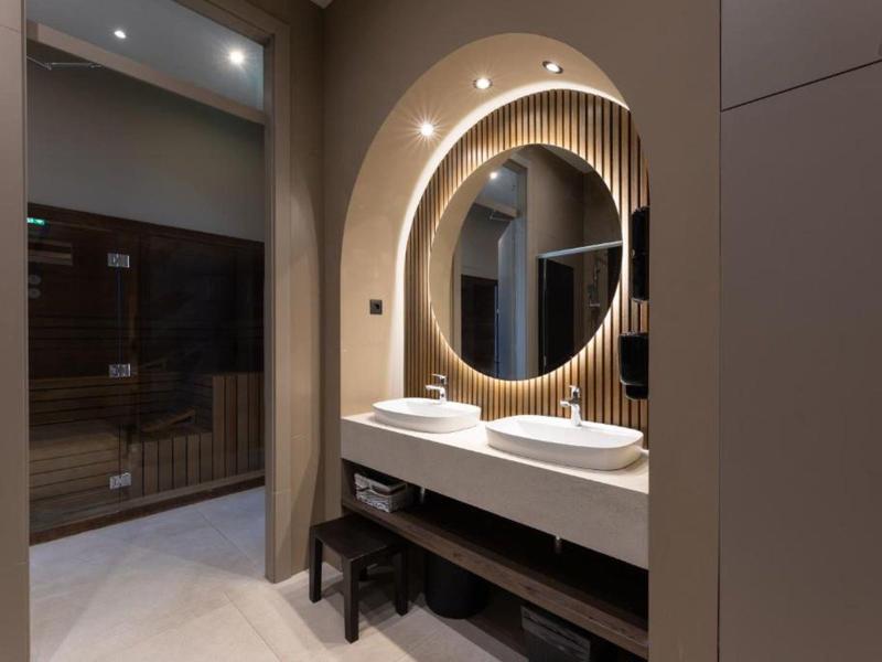 Modernes Badezimmer mit rundem Spiegel, doppeltem Waschbecken und stimmungsvoller Beleuchtung.