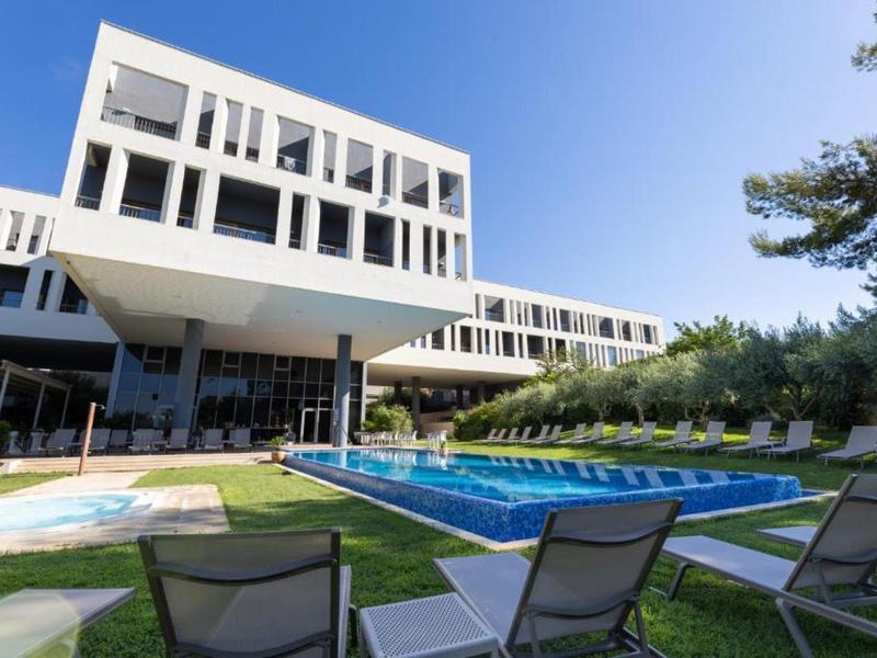 Modernes Hotelgebäude mit Pool, Liegestühlen und klarem Himmel im Hintergrund.
