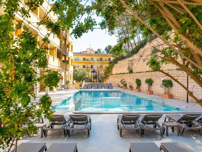 Area piscina esterna con lettini, circondata da edifici e muri verdi.