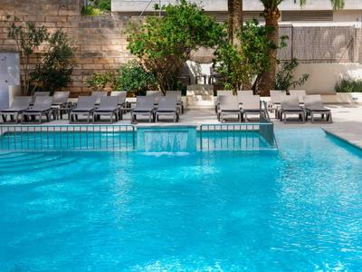 View of a blue pool with lounge chairs and plants in the background.