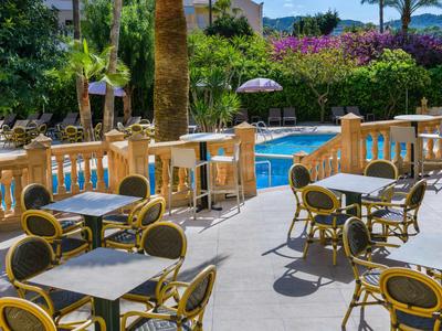 Terrace with tables and chairs next to a pool and palm trees in the background.