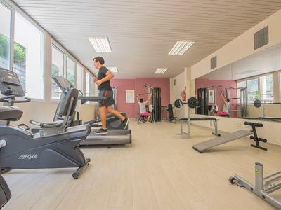 Modern gym with exercise equipment and a person running on a treadmill by the window.