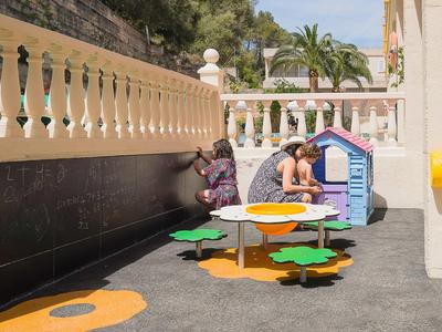 Two children play in an outdoor area with colorful play table and playhouse.