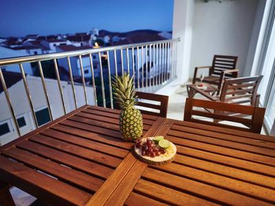 Wooden table on balcony with pineapple and grapes, view of houses at dusk.