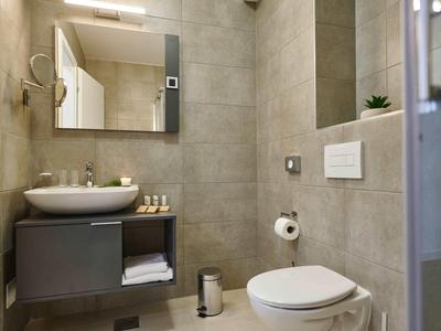 Modern bathroom with gray tiles, sink, toilet, and large mirror.