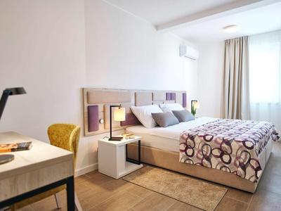 Bright hotel room with double bed, desk, white walls, and brown wooden floor.