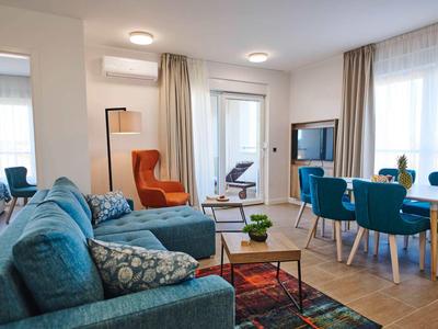Bright living room with blue sofas, orange armchair, and dining area with blue chairs.