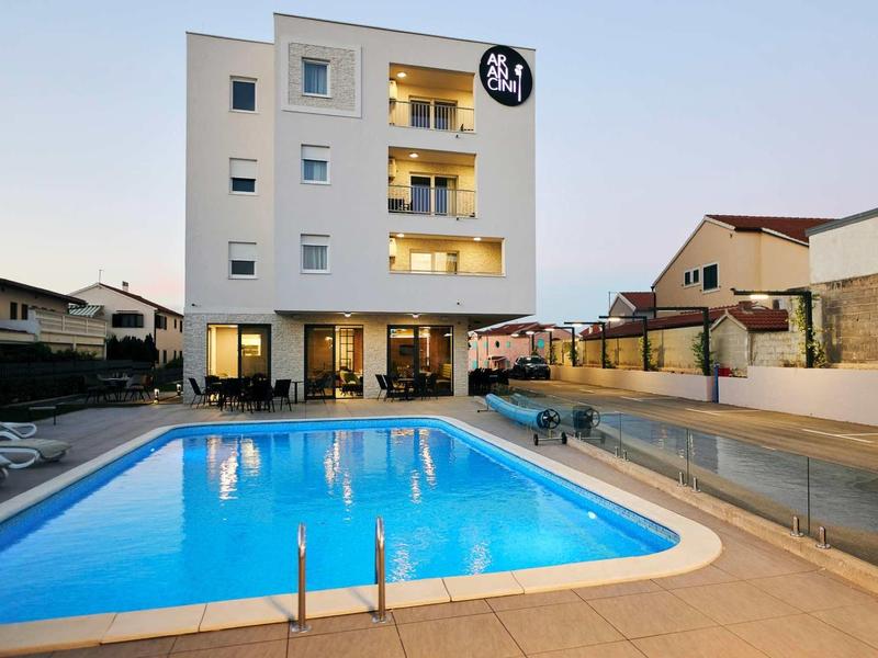 Modern meerlaagse hotel met verlicht zwembad en ligstoelen.