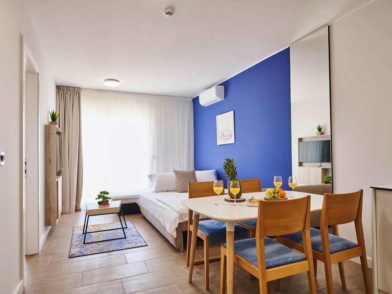 Modern hotelkamer met blauwe accentmuur, eettafel en groot raam.